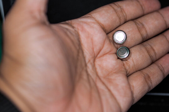 human hand holding two small silver button cell batteries on the palm.