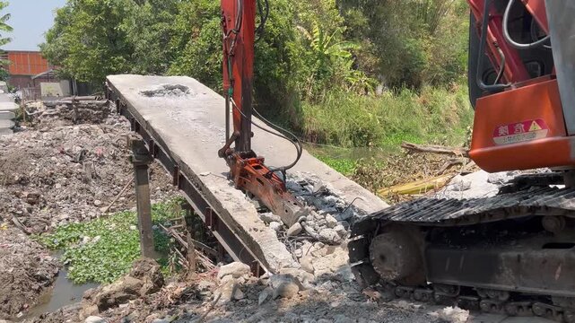 Close up of orange excavator operating hydraulic breaker on demolition site