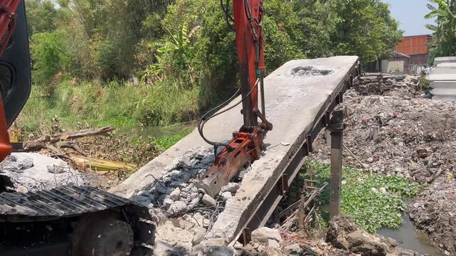 Side view of excavator hydraulic breaker demolishing concrete bridge