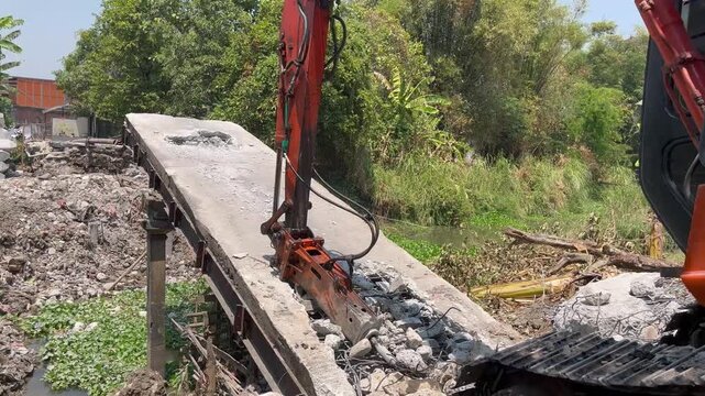 Excavator with hydraulic breaker attachment destroying old concrete bridge