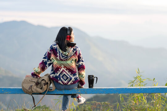Woman relaxing and enjoying the mountain landscape with headphones and reusable cup