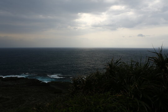 Sunlight breaks through clouds over the vast ocean shore.