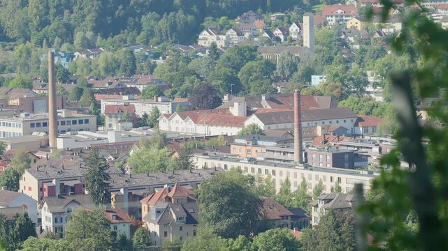 A view of a dense urban area with many buildings and trees. A tall brick chimney stands out among the structures.