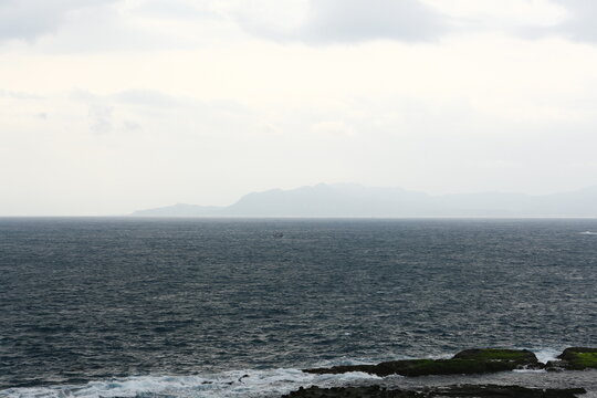 Misty mountains rise beyond the ocean under a cloudy sky.