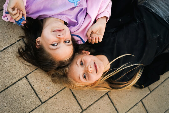 Two happy young girls lying head to head on a brick pavement