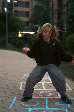 Young girl with flying hair playing hopscotch outside at dusk
