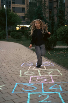 Young girl with long hair playing hopscotch at dusk