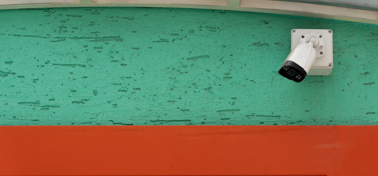 White security camera mounted on a bright turquoise textured wall