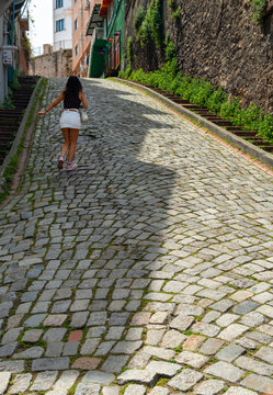 Woman walking up a cobblestone street in Istanbul with historic architecture and greenery along the old city slope