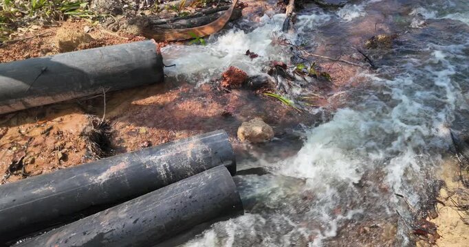 Slow motion close-up of water gushing forcefully from several black industrial pipes into a rocky stream