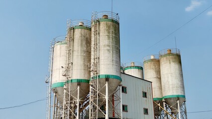 Large industrial storage silos at a processing plant under clear blue sky, representing manufacturing, bulk storage and industrial infrastructure. © Yangkasa
