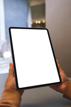 Vertical mockup image of a woman holding digital tablet with blank white desktop screen in cafe