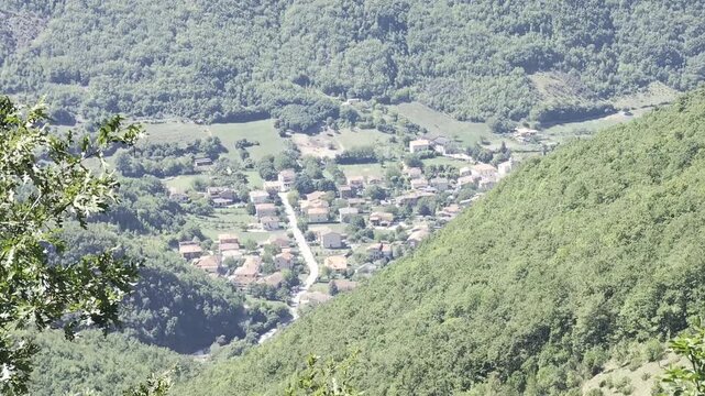 Veduta panoramica di un piccolo borgo appenninico adagiato nella vallata tra fitti boschi e montagne verdi, sotto la luce nitida di una giornata estiva
