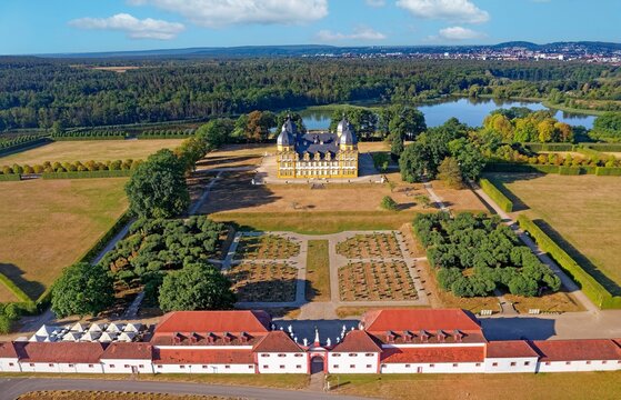 Aerial view of Seehof Castle, baroque palace complex with yellow-white main castle, distinctive corner towers and baroque castle garden with hedges and trees, lakeside area and city skyline under slightly cloudy blue sky, Memmelsdorf, Bamberg district, Upper Franconia, Bavaria, Germany
