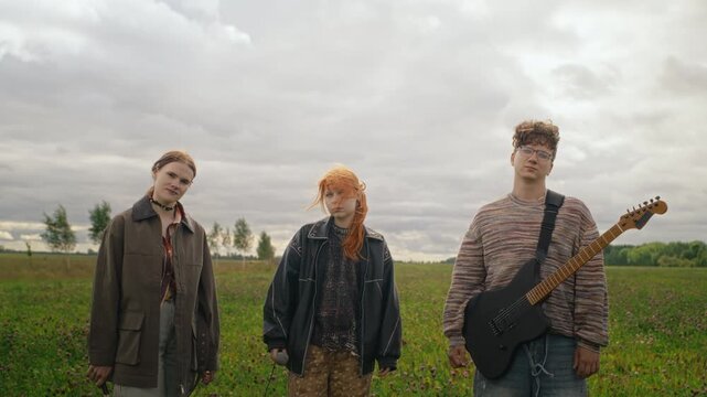 Portrait of young adult Caucasian indie band members standing in field with electric guitar and drumsticks. Footage suitable for youth culture marketing or music festival promotion