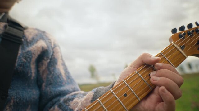 Caucasian young man playing electric guitar outdoors in green meadow. Clip ideal for indie band music videos, youth lifestyle advertising, audio equipment promos, and concert teasers