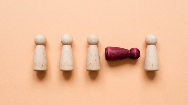 One wooden figure lying down among standing figures symbolizing failure or exclusion in team concept