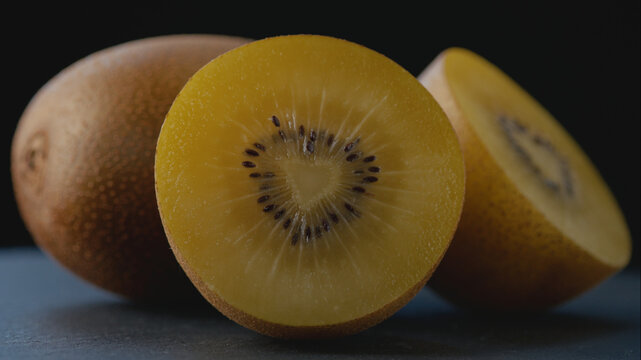 Macro shot of a golden kiwi cut in half showing a heart-shaped core, with another half and whole kiwi on dark background with studio lighting for healthy eating, gourmet food, and culinary content.