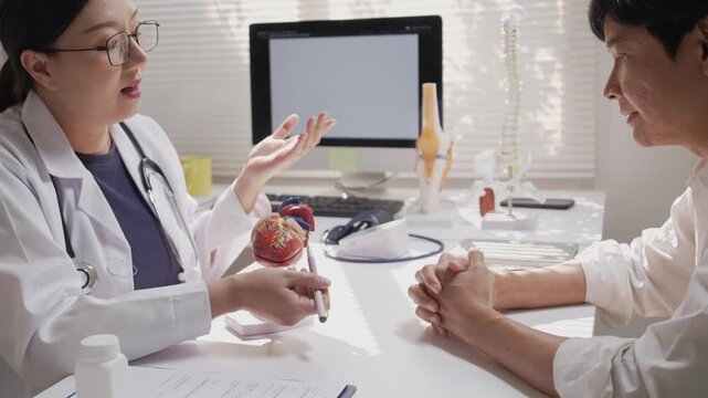 Asian Female Cardiologist Explaining Heart Anatomy using Model to Patient during Medical Consultation