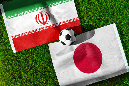 Iran vs. Japan football match. National flags on green grass with soccer ball in the middle. Football background for international match.