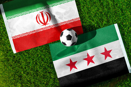 Iran vs. Syria football match. National flags on green grass with soccer ball in the middle. Football background for international match.