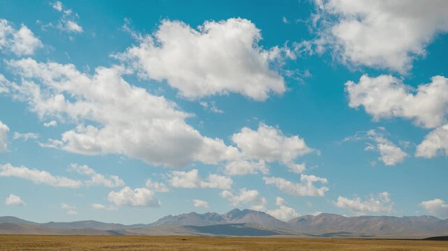 White clouds are moving quickly across the blue sky above the mountains, time‑lapse