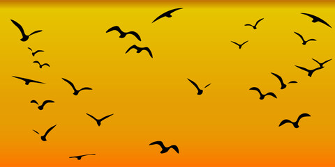 Fototapeta premium The silhouette of a flock of black birds in flight against a sky with yellow and orange color gradients, resembling a sunset scene.