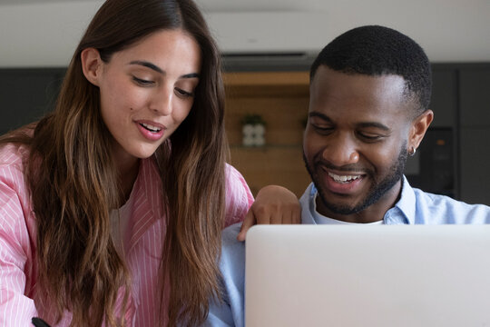 Young couple smiling as they shop online on a laptop at home, discussing purchases and comparing options while enjoying a relaxed, collaborative moment of planning and budgeting.
