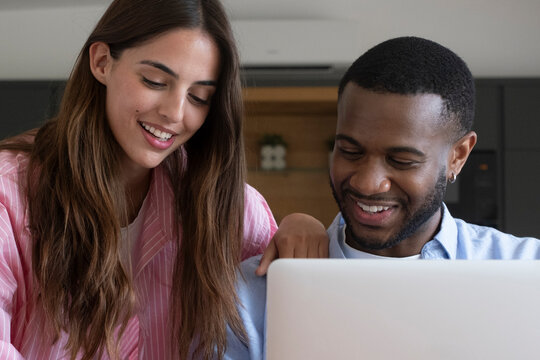 Young couple smiling and researching travel insurance online on a laptop at home, collaborating on plans with relaxed, happy expressions and a cozy weekend atmosphere and planning.
