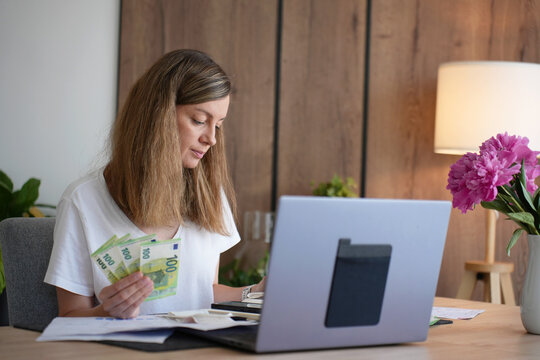 Woman managing household budget with euro cash and laptop at home