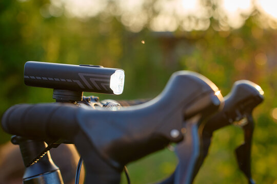 Close-up of a bicycle front light turned on above the handlebars at sunset