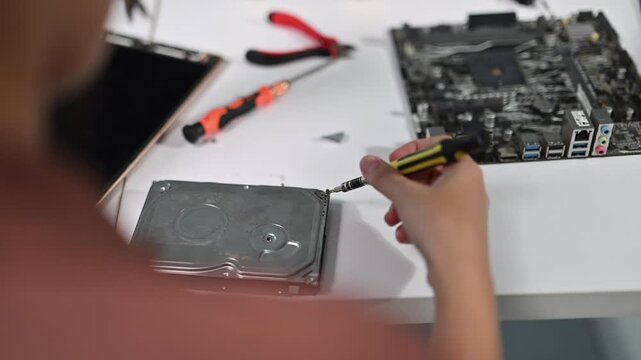 Person repairing computer components with screwdriver and tools on table
