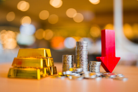 Financial crisis and market downturn concept with stacked gold bullion bars, coin stacks and red downward arrow on table for economic inflation hedge, currency devaluation and wealth safety.