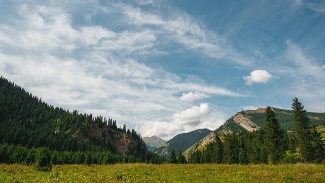 White clouds are moving quickly across the blue sky above the mountains, time‑lapse.