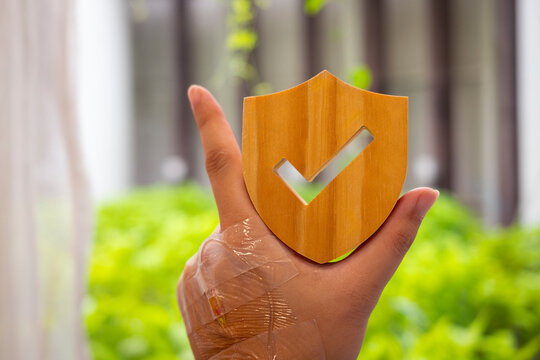 Hospital health insurance and patient recovery concept with iv catheter taped hand holding wooden shield with checkmark for medical reimbursement claim approval and healthcare guarantee.