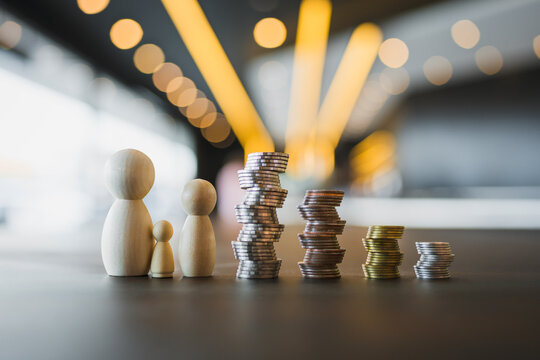 Family wealth accumulation and child savings concept with wooden peg doll figures beside rising coin stacks on table for household budget, education fund and generational financial planning.