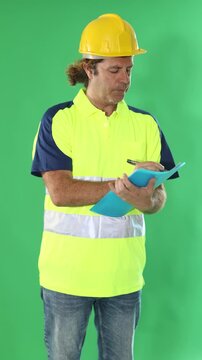 Road service worker in a protective helmet and a reflective polo makes notes in documents against the background of chromakey . High quality 4k footage
