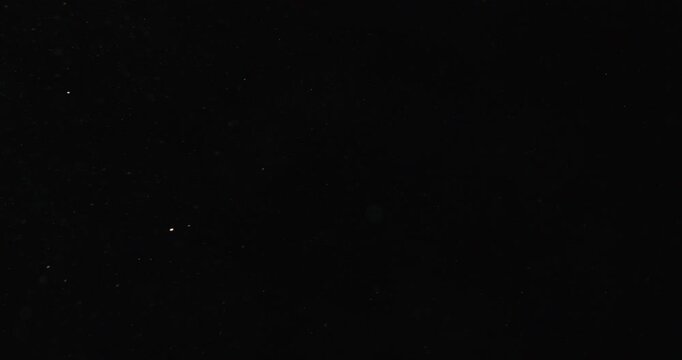 Tiny snow or dust randomly flying in the smoky air, empty space template for objects advertisement. Many dust particles cloud of white powder in low light on empty dark black contrast background.