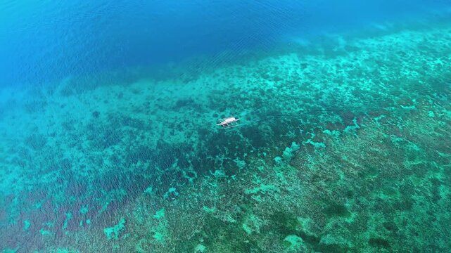 Small traditional outrigger boat floating on turquoise coral reef