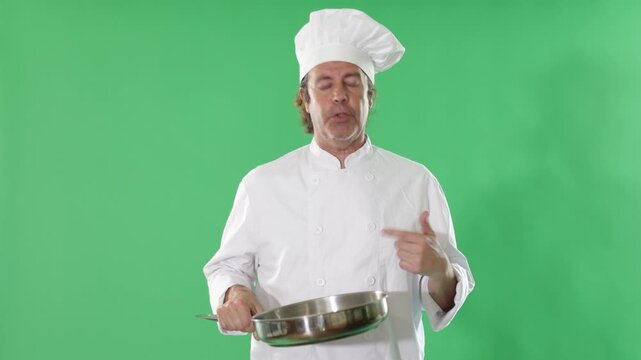 Experienced chef holds a frying pan in his hands against the background of a chromakey. Qualified cook invites to a master class on cooking breakfast on a green background . High quality 4k footage