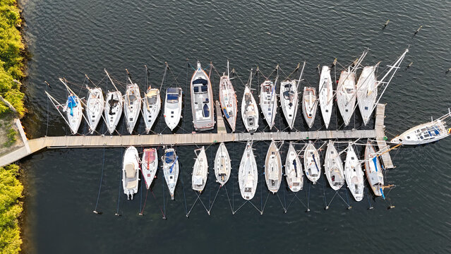 Yachthafen mit dicht an dicht liegenden Segelbooten am Holzsteg, aufgenommen aus der Luft bei ruhigem Licht und dunklem Wasser. Authentische Luftaufnahme / Drohnenfotografie einer Marina