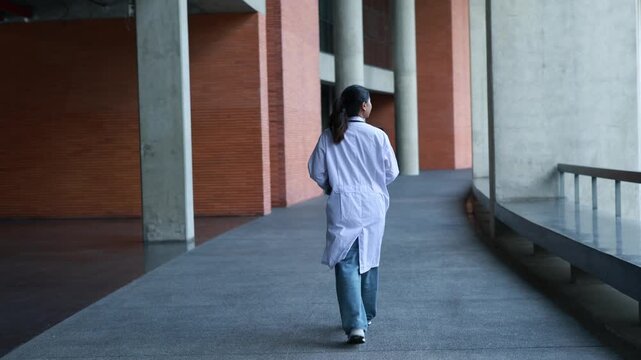 Rear view Asian female medical students walk modern university or medical school building wearing their medical uniforms signifying their dedication education and new beginning.