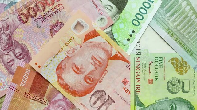Close-up rotating various Asian currency banknotes including Singapore dollars, Vietnamese dong, Indonesian rupiah, and UAE dirham