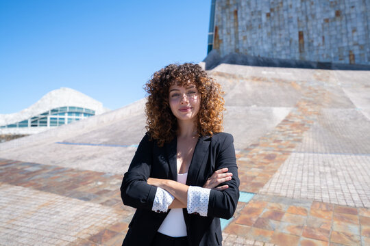 Businesswoman with curly hair posing confidently outdoors