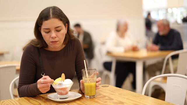 Food court girl visitor sits near table, eating ice cream in chain cafe shop. Coffee shop or coffee house, girl resting at table 