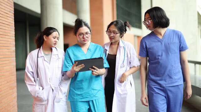 Group of friends : Group asian medical students dressed in blue scrubs and white coats walk and converse with one another on the campus of a modern university.

