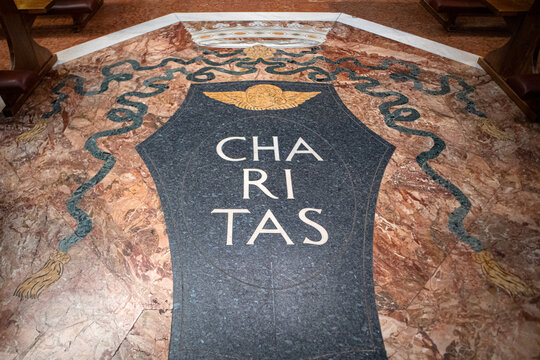 Iscrizione in latino Charitas intarsiata nel pavimento in marmo policromo all'interno di una chiesa storica, simbolo cristiano di carit&agrave;, amore e devozione spirituale.