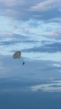 Silhouette of a person parasailing high above the sea against a cloudy blue evening sky