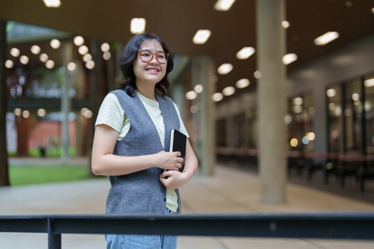 Smiling student holding notebook standing on campus