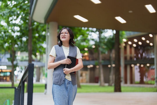Asian female student walking on campus with books